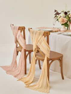 two wooden chairs sitting next to each other near a table with white cloth draped over it