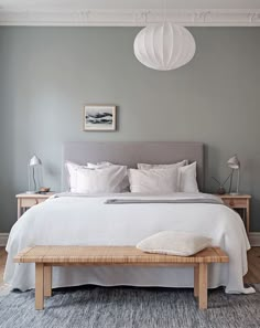 a bed with white sheets and pillows in a bedroom next to a wooden foot board