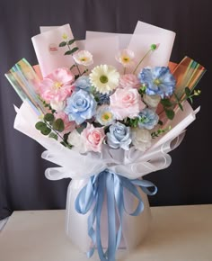 a bouquet of flowers in a white vase with blue and pink ribbons on the side