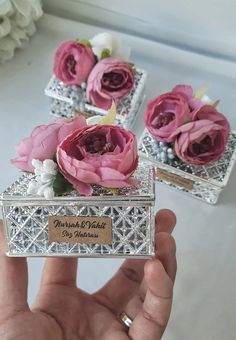 a hand holding a silver box with pink flowers in it and three other boxes behind it