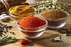 three bowls filled with different types of spices on top of a wooden table next to herbs