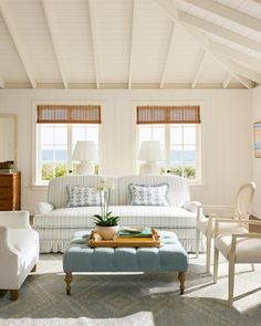 a living room with white furniture and blue accents on the walls, along with two windows