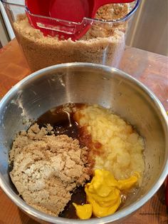 ingredients in a metal bowl on a wooden table next to a measuring cup and spoon