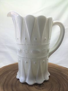 a white ceramic pitcher sitting on top of a wooden table next to a white wall