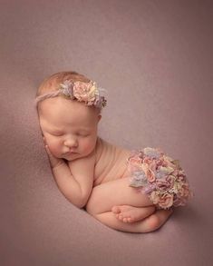 a baby is laying down with her hands on her chest and wearing a flower headband