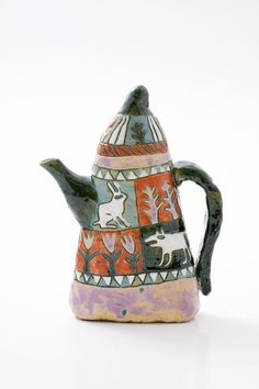 a ceramic teapot with an animal design on the front and side, sitting on a white surface