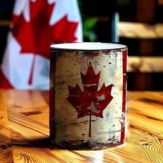 a red and white maple leaf painted on an old tin can sitting on a wooden table