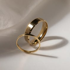 two gold wedding rings sitting on top of each other