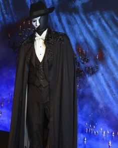 a man in a black suit and top hat with a mask on his face, standing next to a stage backdrop