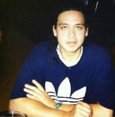 a young man sitting at a table with his arms crossed and wearing a blue shirt