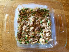 a glass casserole dish filled with chicken, peas and corn on a wooden table