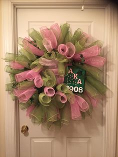 a pink and green mesh wreath hanging on the front door with a house number sign