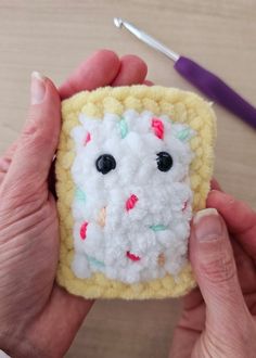 someone is holding up a small crocheted square that has been made into a face