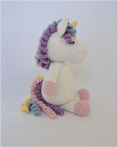 two crocheted stuffed unicorns sitting next to each other on a white surface