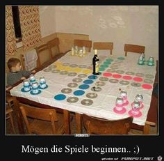 a child sitting at a table with cups and bottles on it, in front of a sign that says mogen die spiel beginen