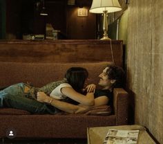 a man and woman laying on a couch in a living room next to a lamp