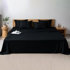 a bed with black sheets and pillows in a room next to a plant on the floor