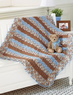 a teddy bear sitting on top of a bed under a blue and brown crocheted blanket