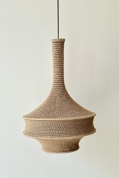 a woven light fixture hanging from a white wall with a black cord attached to it