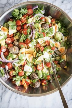 a salad with meatballs, tomatoes and lettuce in a bowl on a marble table