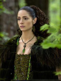 a woman in a green dress standing in the woods with her hair up and eyes closed