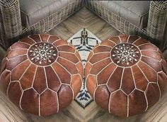 two brown leather ottomans sitting on top of a wooden floor next to wicker chairs