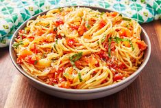 a bowl full of pasta with tomatoes and parmesan cheese on the top, sitting on a wooden table