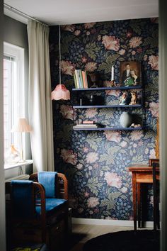 a living room with floral wallpaper and blue chair in front of the window,