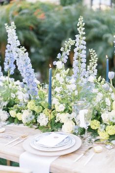 the table is set with blue and white flowers, candles, and plates on it