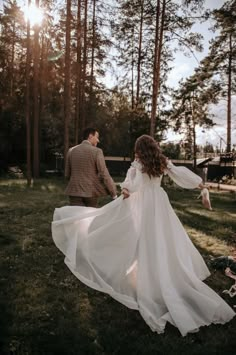 a bride and groom walking through the woods