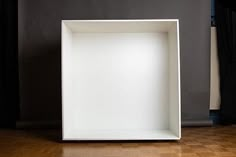 an empty white box sitting on top of a hard wood floor in front of a black wall