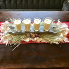 three candles on a tray with feathers and pine cones