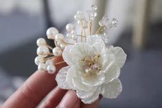 a close up of a person's hand holding a flower and pearl brooch