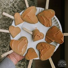 a person holding a paper plate with heart shaped cookies on skewers in front of them