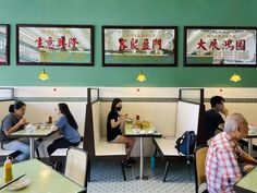 people sitting at tables in a restaurant with chinese writing on the walls and posters above them