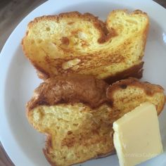 two pieces of bread on a white plate with butter and a piece of cheese next to it