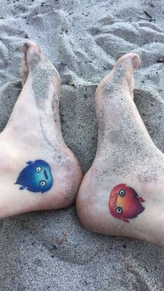 two feet with tattoos on them laying in the sand