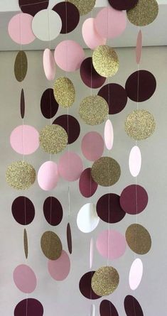 some pink and gold paper circles hanging from the ceiling in front of a white wall