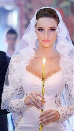 a woman in a wedding dress holding a candle with her hands and looking at the camera