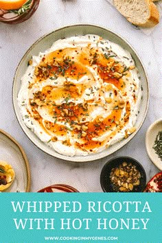 whipped ricotta with hot honey in a bowl surrounded by bread, oranges and other food