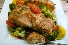 a white plate topped with fish, broccoli and cherry tomatoes next to a fork