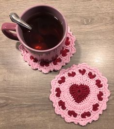 two crocheted coasters on a table with a cup of tea in the middle