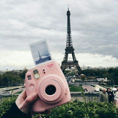 a person holding up a pink camera in front of the eiffel tower