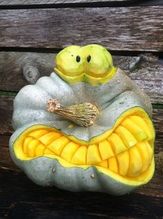 a pumpkin shaped like a snake sitting on top of a wooden bench with its mouth open