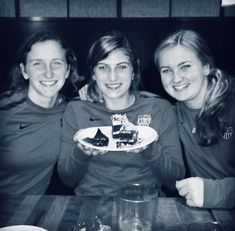 three young women sitting at a table with plates of food