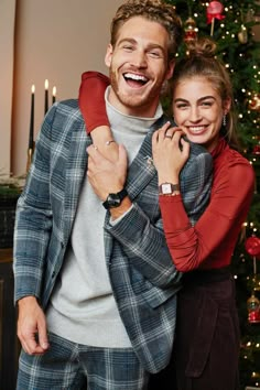 a man and woman standing in front of a christmas tree with their arms around each other