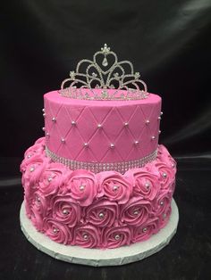 a three tiered cake with pink frosting roses and a tiara on top