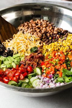 a large metal bowl filled with different types of salads and ingredients to make it