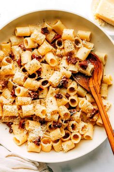 a white bowl filled with pasta and meat on top of a table next to a wooden spoon