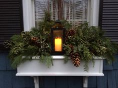 a window sill filled with pine cones and greenery next to a lit candle